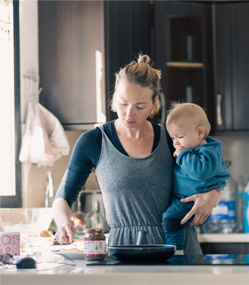 Busy mom cooking while caring for a child before switching to convenient meal prep services.